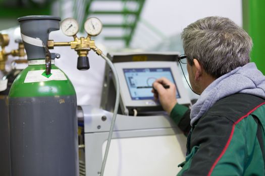 Industrial operator setting  computer controlled process of orbital welding machine in inox pipes manufacturing workshop.