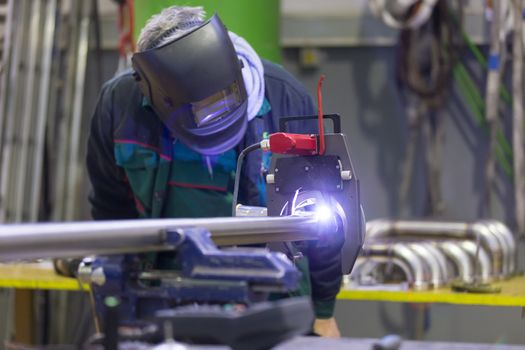 Industrial operator setting  computer controlled process of orbital welding machine in inox pipes manufacturing workshop.