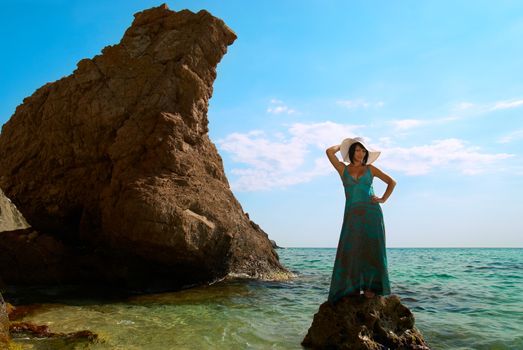 Pretty woman in dress and hat on the sea rock