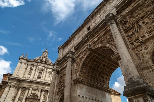 Bottom view of ancient arch with columns at Roman Forum, on cloudy blue sky background.