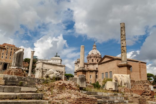 View of archeological area of ancient Roman Forum in Rome, on cloudy blue sky background.