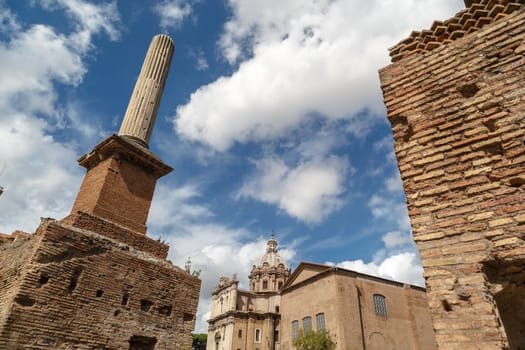Detailed view of column in ancient Roman Forum in Rome, on cloudy blue sky background.