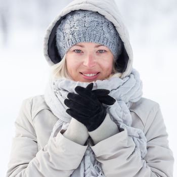 Girl wearing gloves, beeing cold outdoors in winter. Beautiful winter portrait of young woman in the winter snowy scenery.