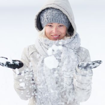 Cute casual young woman playing with snow in winter time.