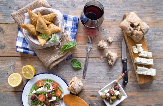 Feta cheese and spinach filo pastries and greek salad laid out on a wooden table 