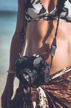 Woman on a tropical beach with an film camera around her neck.