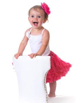 happy one year old girl wearing tutu standing on a white chair