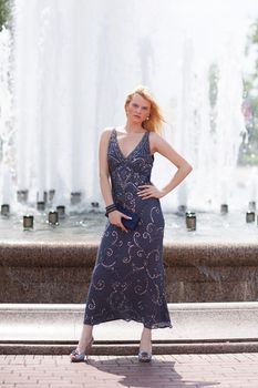 Blond woman in glitter dress next to fountain цшер purse
