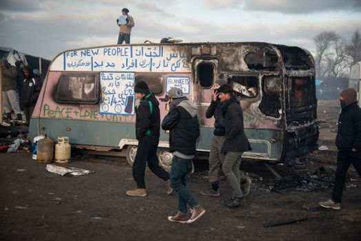 FRANCE, Calais: Just-evicted refugees walk past a burned-out home as authorities dismantle the 'Jungle' migrant camp in Calais, France on February 29, 2016. Residents of the controversial site in this northern town are being relocated as a new camp is being built. In protest, some set fire to the temporary homes at the camp.