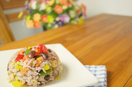 Fried rice vegetarian include eringi mushrooms carrots and corn with blue fabric on wood table and blur flower as background.