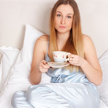 Woman in pajamas holding cup of teaon her bed