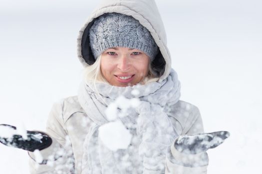 Cute casual young woman playing with snow in winter time.