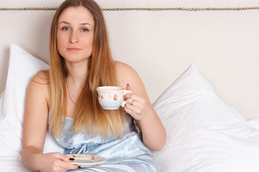 Woman in pajamas holding cup of teaon her bed