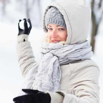 Cute casual young woman snowball fighting in winter time.