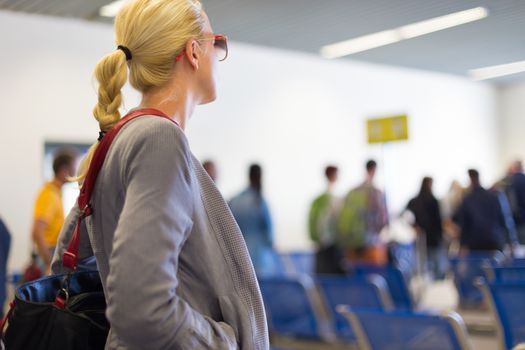 Young blond caucsian woman waiting in line. Lady standing in queue to board a plane.