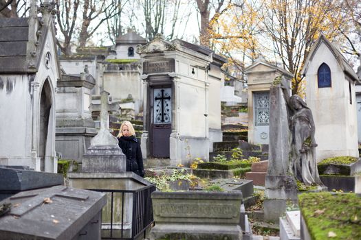 Solitary woman mourning by gravestone, remembering dead relatives in on Pere Lachaise cemetery in Paris, France.