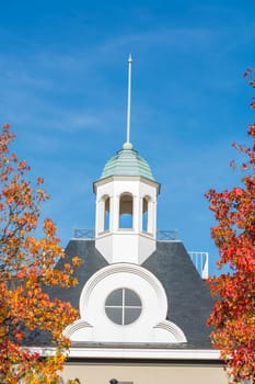 Spire right and left two trees with autumn leaves against blue sky.