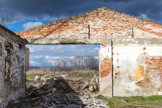 Triangle with visible bricks of the frontage of an abandoned house without a roof. Dirt everywhere in the former room. Visible nature and cloudy sky.