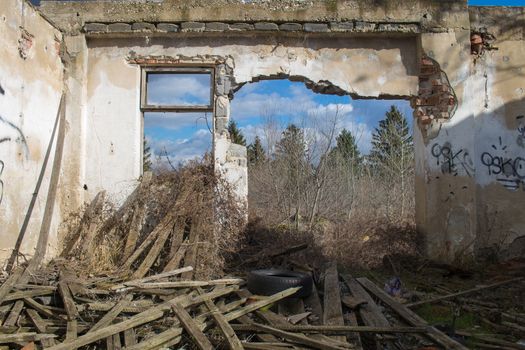 View from the room of an abandoned house, with a broken wall, showing the trees and cloudy sky outside.