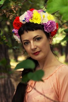 charming woman in wreath of roses on her head on the background of nature