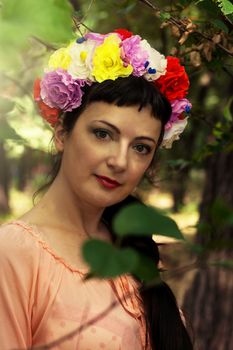 charming woman in wreath of roses on her head on the background of nature