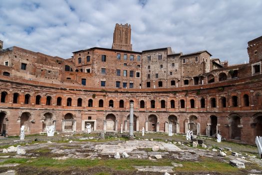 View of an ancient Roman Forum with columns and ruins around in Rome, with tourists around, on cloudy sky background.