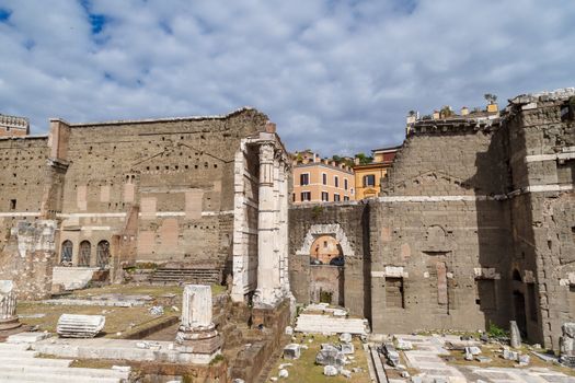 View of an ancient Roman Forum with columns and ruins around in Rome, with tourists around, on cloudy sky background.