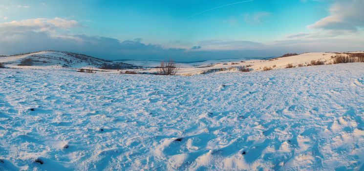 Panorama with winter hills covered by snow against sunset