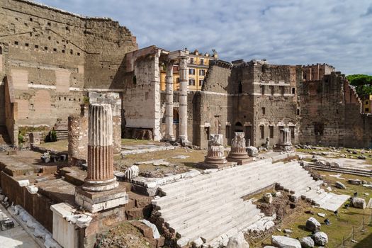 View of an ancient Roman Forum with columns and ruins around in Rome, with tourists around, on cloudy sky background.