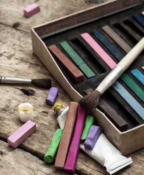 Crayons and paints for painting on wooden background