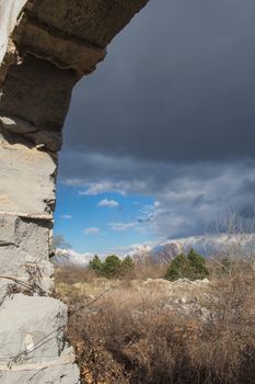 Frame of the former door of an abandoned house. Early spring nature and stormy weather sky.