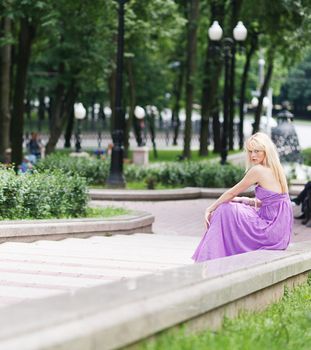 Blond girl in fashion dress sitting on stairs