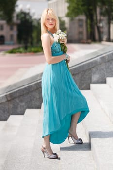 Blond Girl stand on stairs with flower on hand in fashion dress