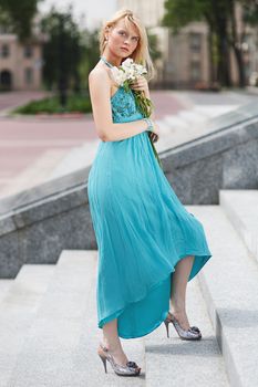 Blond Girl on stairs with flower on hand in fashion dress