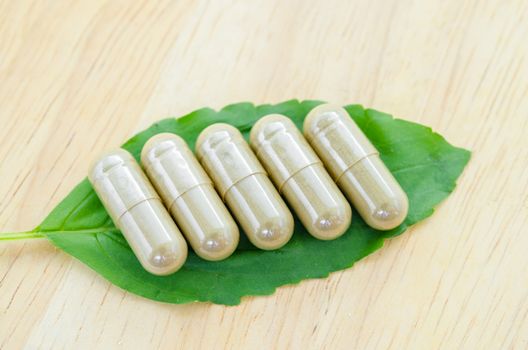 Herbal medicine capsules with green leaf on wooden background.