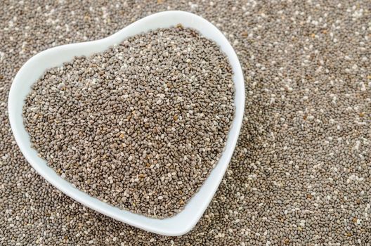 Chia seeds in white bow heart shape on chia seeds background.