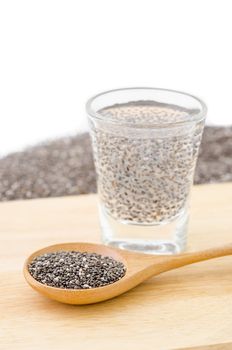 Wooden spoon of chia seeds with chia seeds soaking in a glass of water.