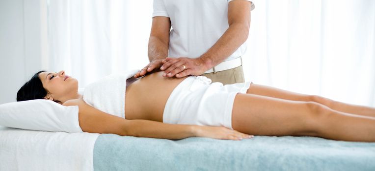 Pregnant woman receiving a stomach massage from masseur at home