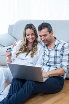 Expecting couple sitting on sofa and using laptop