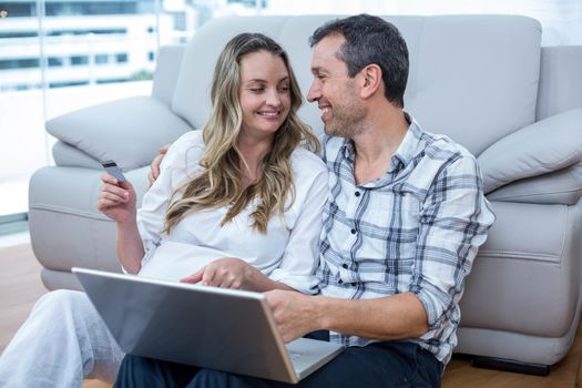 Expecting couple sitting on floor and using laptop