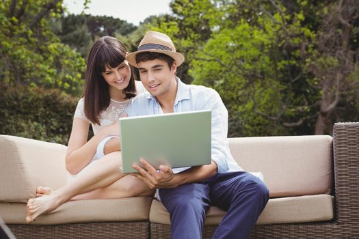Young couple looking at laptop while sitting outdoors on sofa