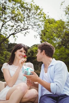 Man giving surprise gift and a rose to woman outdoors