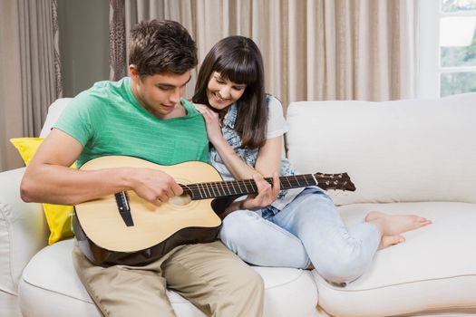 Romantic couple at home playing guitar on the sofa in their living room