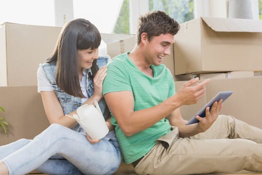 Young couple eating noodle and using digital tablet in their new house