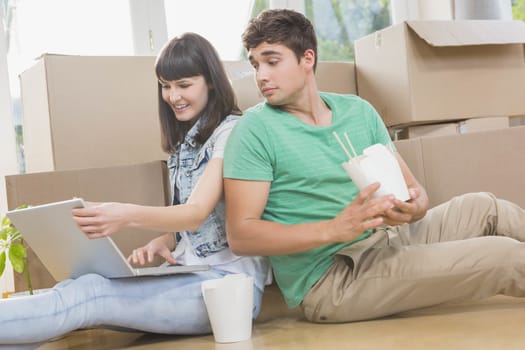 Young couple eating noodle and using laptop in their new house