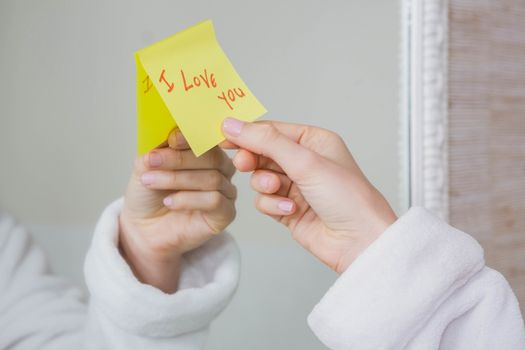 Woman sticking I love you word sticky note on mirror