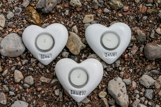 Set of heart shaped candle holders on a pebble river side.