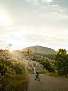 View of nice young woman riding cycle during summer sunset