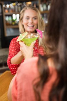 Cute friends toasting with a glass of cocktail in a pub