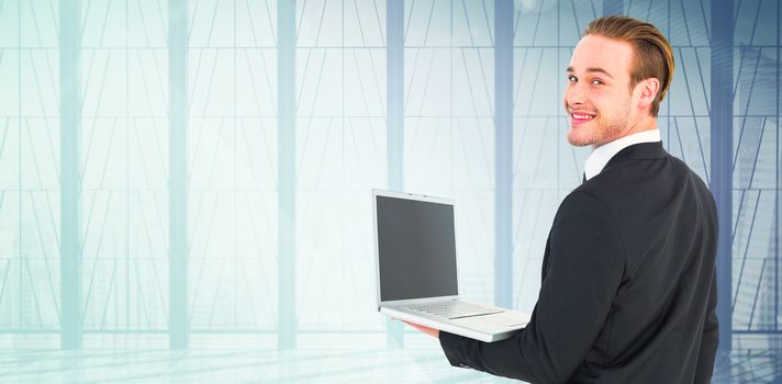 Businessman looking at camera holding laptop against window overlooking city